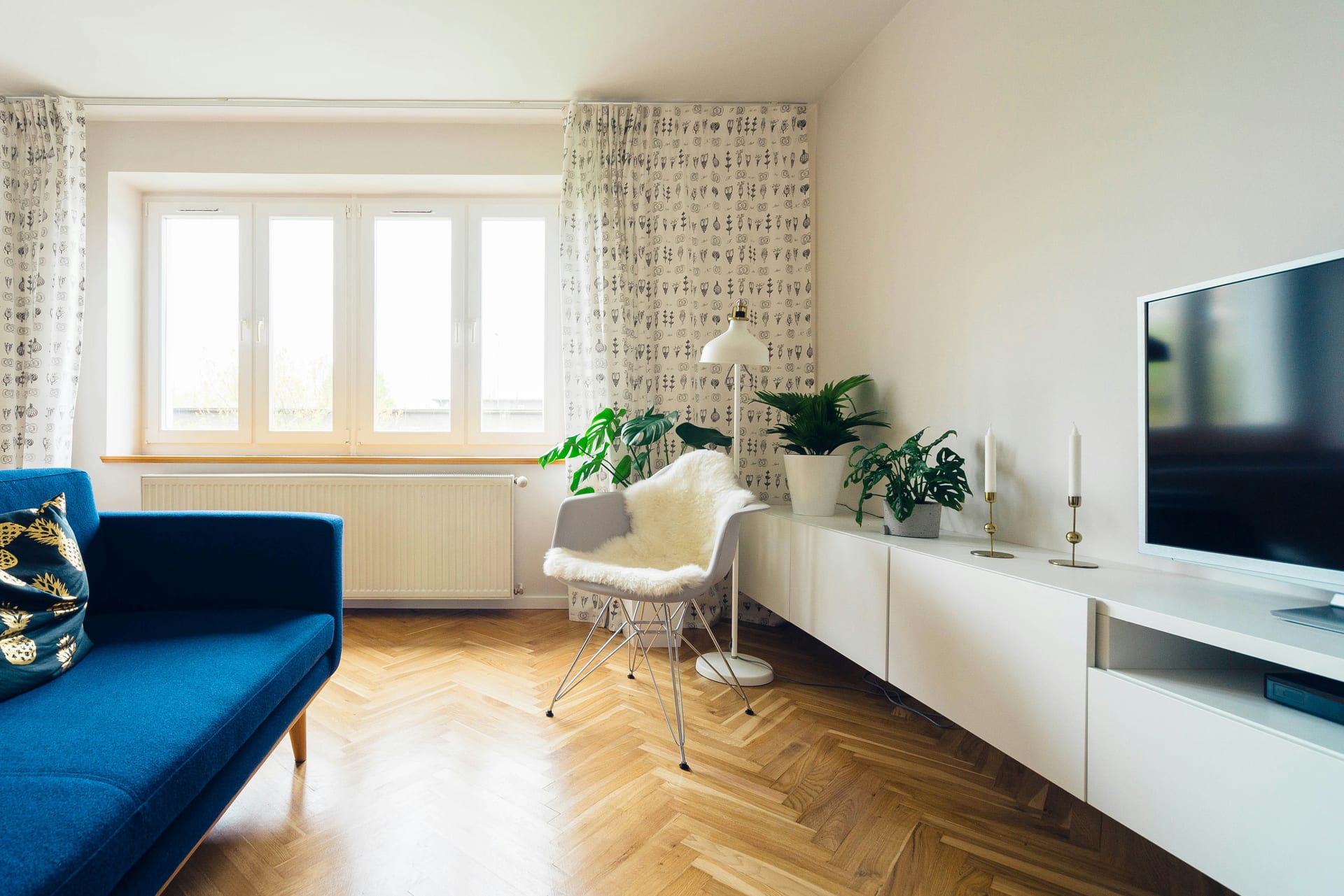 A bright living room with herringbone flooring and a clean, uncluttered sideboard
