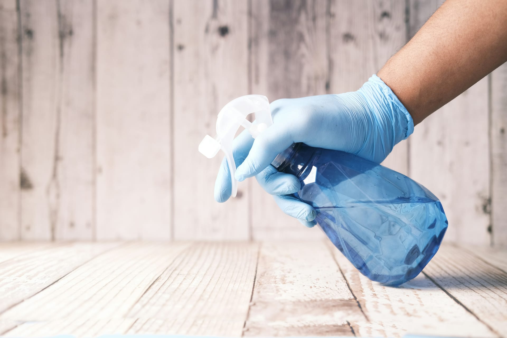 A gloved hand holding a spray bottle beside a freshly wiped surface
